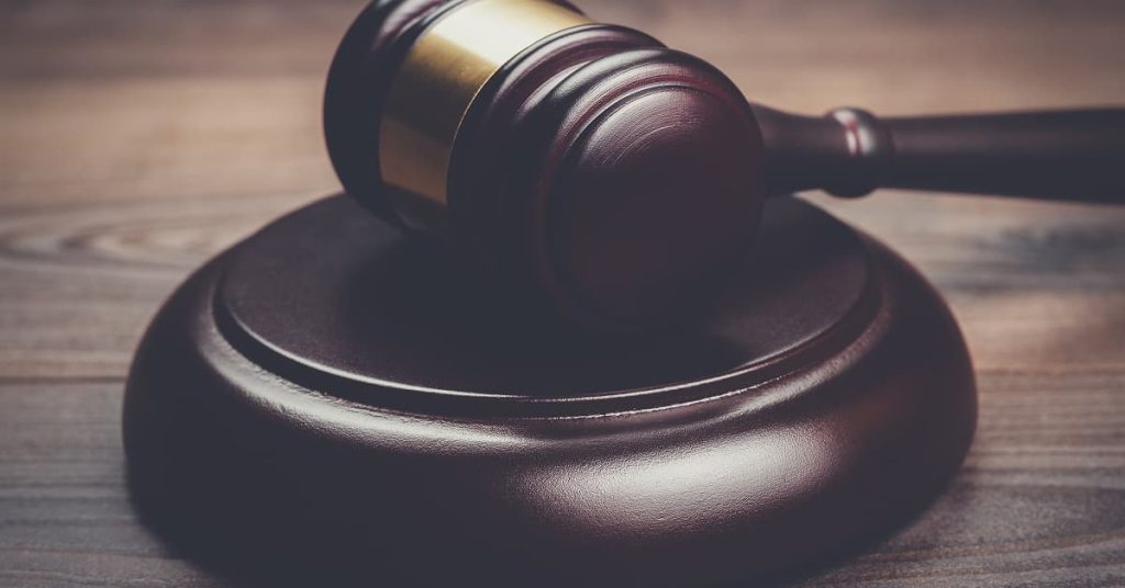 A detailed close-up of a wooden judge’s gavel resting on its sound block atop a polished wooden surface. The gavel’s brass band gleams under soft lighting, symbolizing authority, justice, and courtroom decisions.